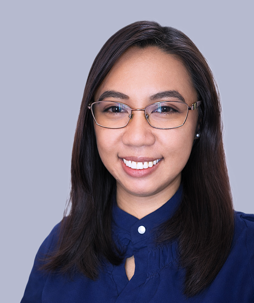 A woman with straight dark hair and glasses smiles at the camera. She is wearing a navy blue blouse and is posed against a plain, light gray background.